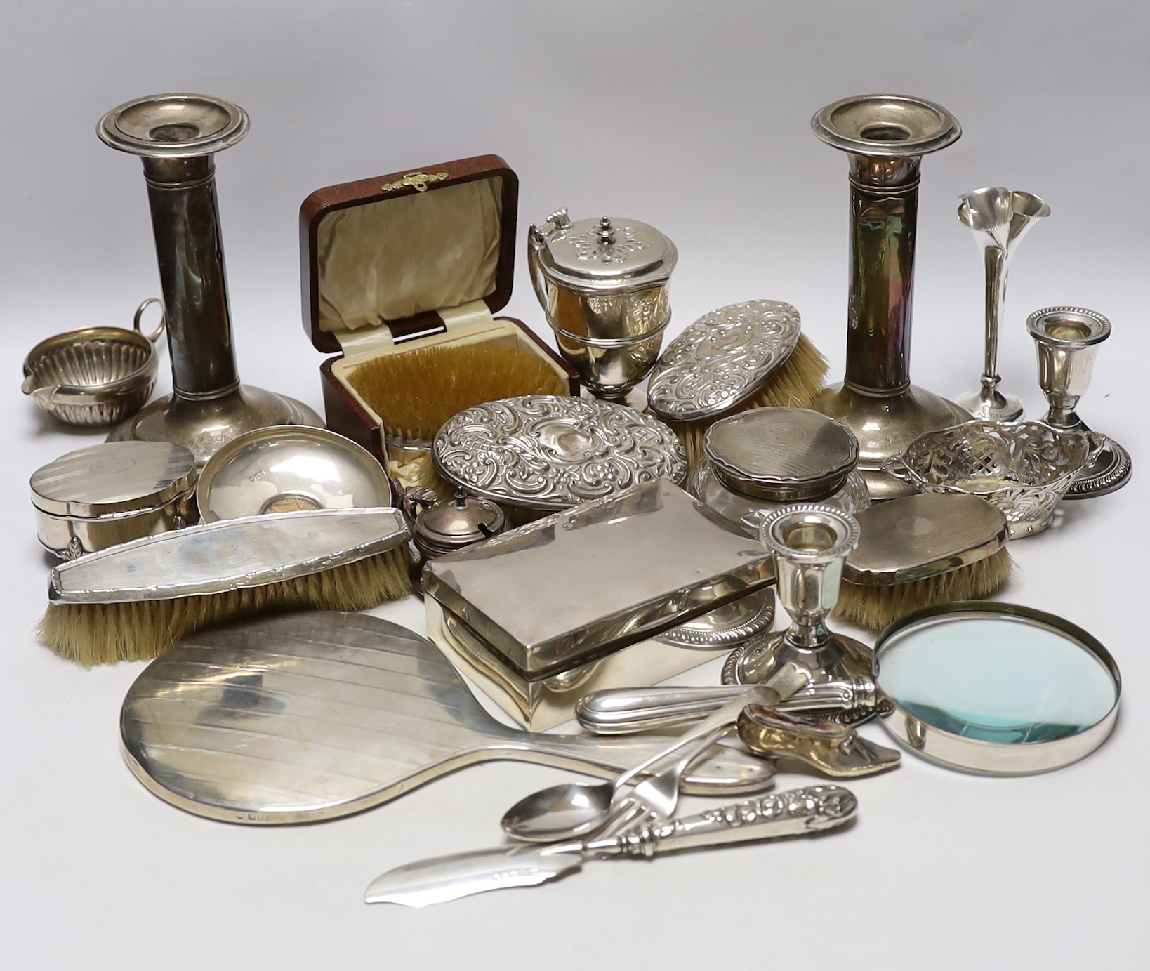 Sundry silver items including a pair of candlesticks, marks rubbed, handled magnifying glass, lidded vase, hand mirror, five brushes, cigarette box, trinket box, toilet jar and eleven other items including a novelty shoe